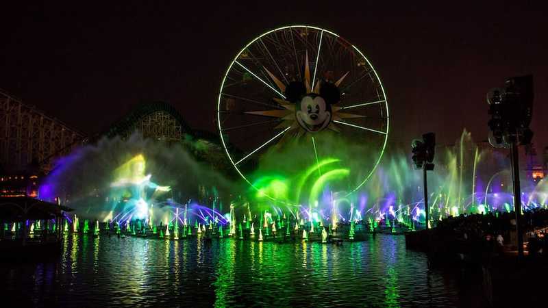 Parque tematico con espectaculo de luces en un lago y una rueda de la fortuna con mickey mouse