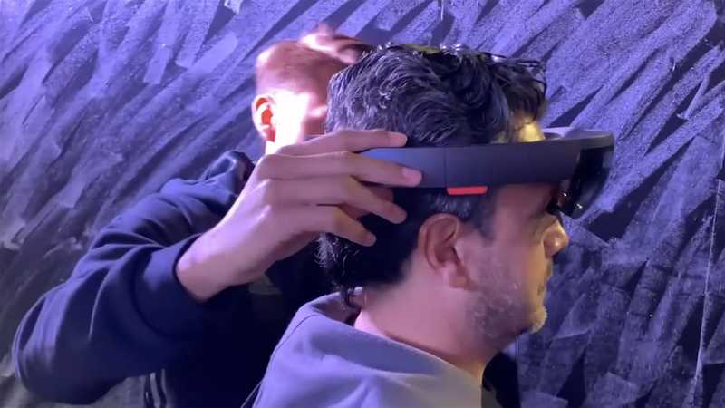 Technician placing a Microsoft Hololens augmented reality helmet over the head of an user.